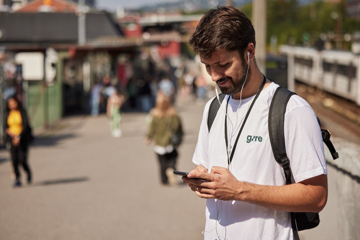 Gire-sjåfør i hvit Gire-t-skjorte som sjekker telefonen på en travel togstasjon