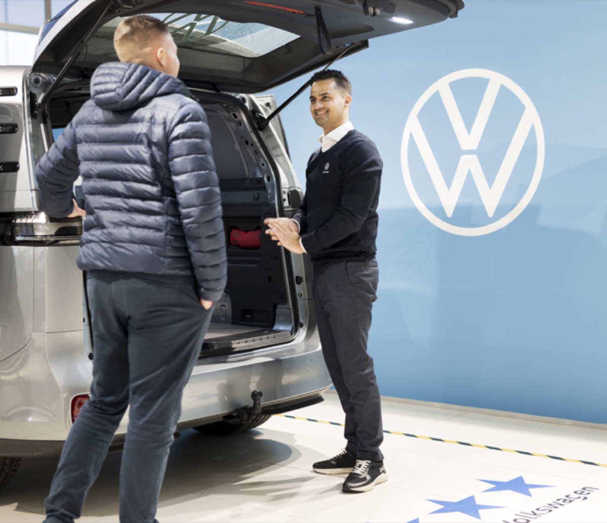 VW-sælger der præsenterer en varebil med åben bagklap for en kunde i en Volkswagen-forhandler